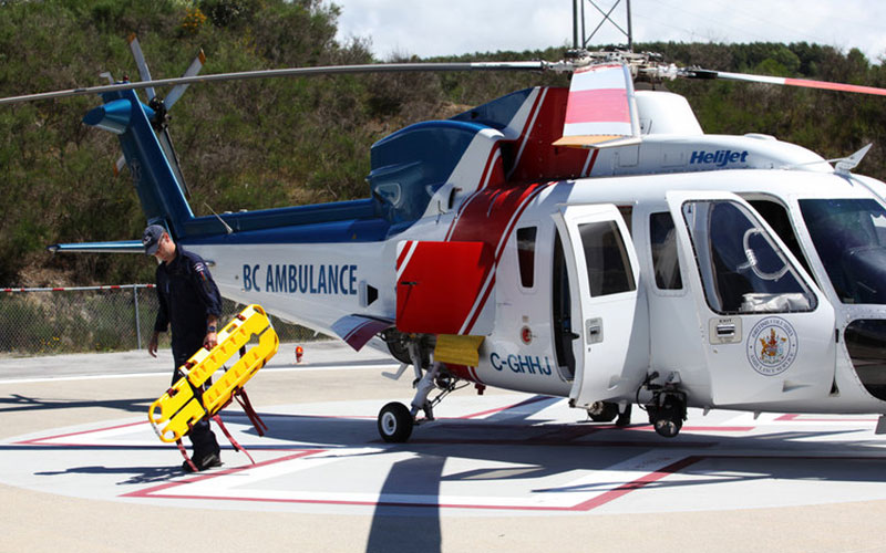 Urgent-Projects-final Medical professional walking away from a BC Ambulance helijet, carrying a yellow stretcher
